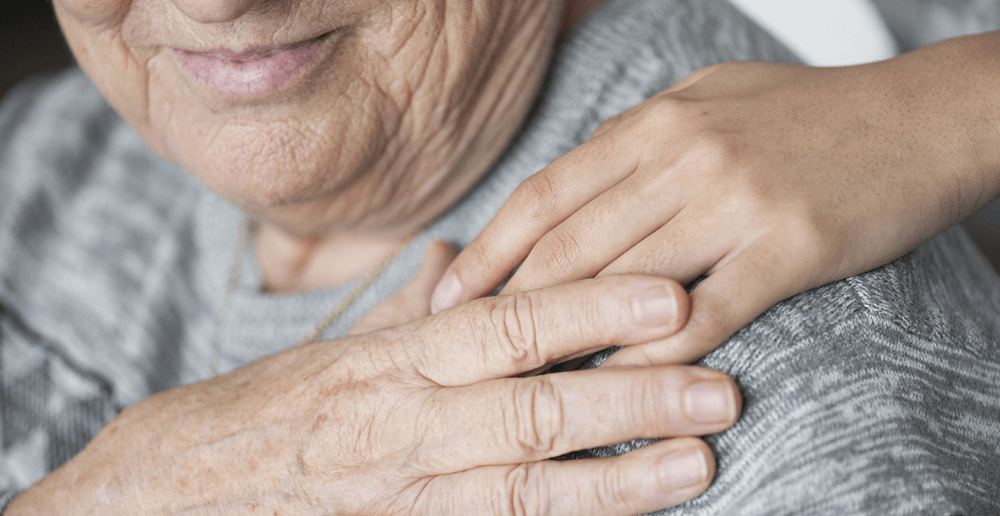 Photo of an elderly woman holding the hand of her younger family member.