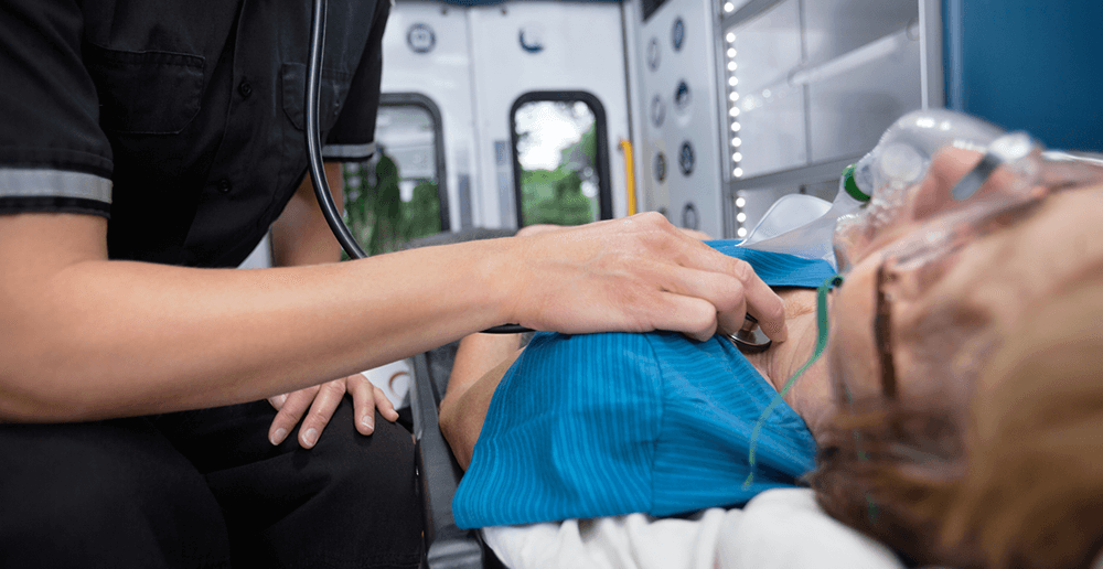 Photo of an EMT worker listening to heart of a patient in an ambulance.